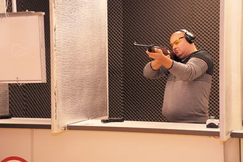 Cursant ochind cu pistolul în cabina de tragere